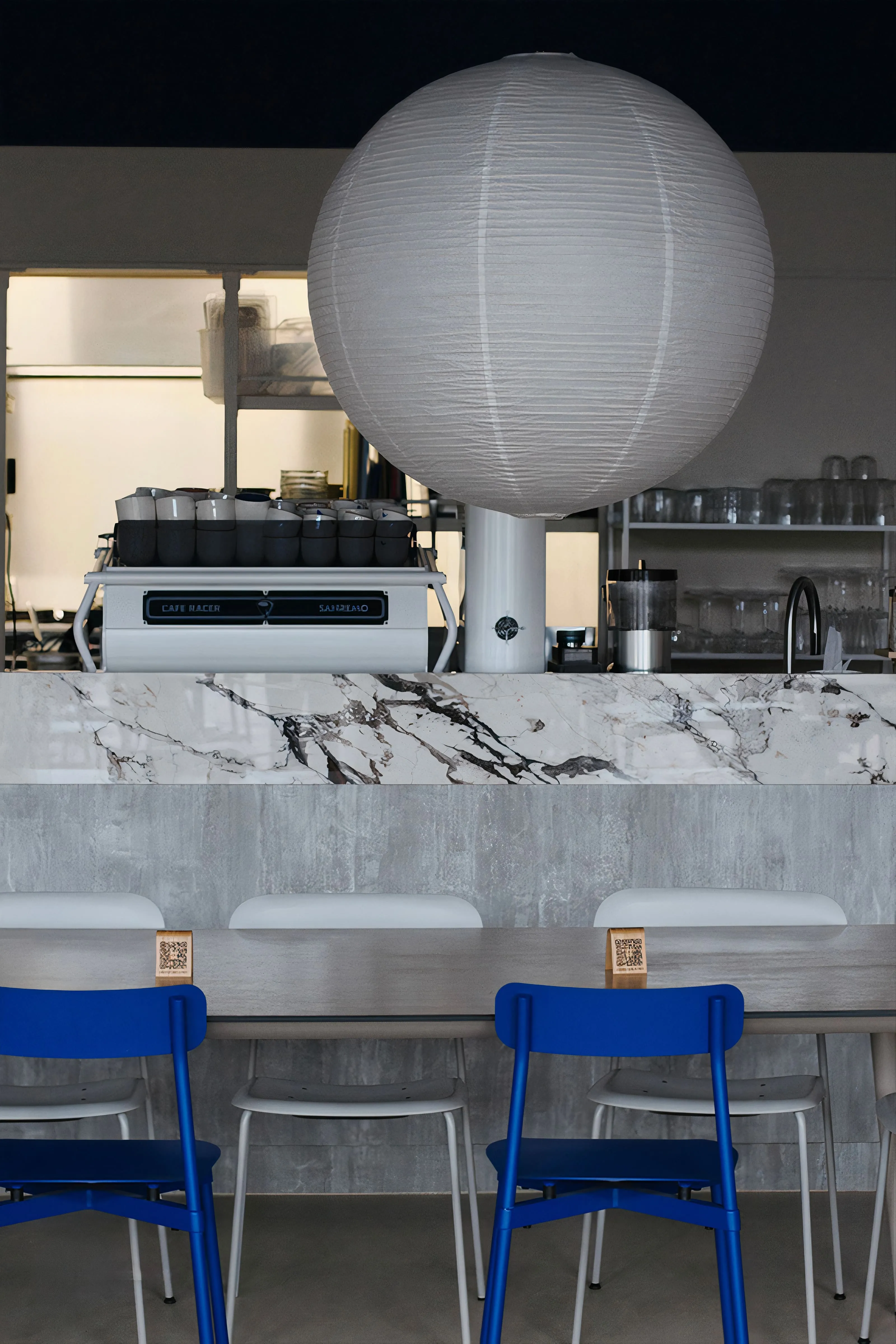 Inside BQ Canteen: blue chairs at a long concrete table under a marble wall